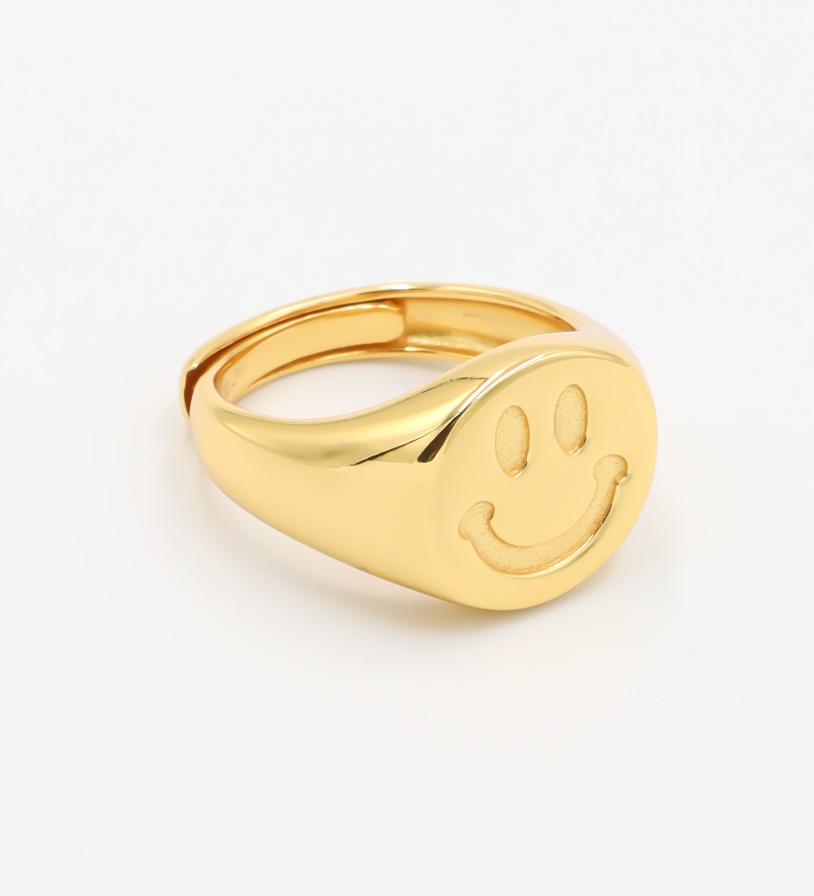 A gold-colored ring with a smiley face design on the top surface.