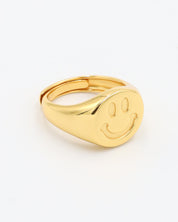 A gold-colored ring with a smiley face design on the top surface.