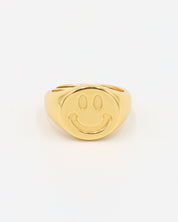 A gold-colored ring with a smiley face design on the top surface.