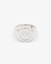A silver ring with a solid pattern and a rounded band, displayed against a white background.