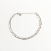 A silver bracelet with two chain layers and heart-shaped charms on it, displayed against a white background.