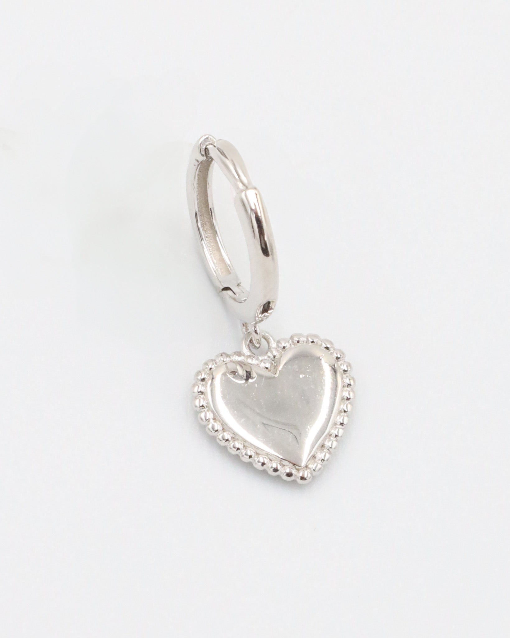 A single silver hoop earrings with heart-shaped pendants attached to them, displayed against a white background.