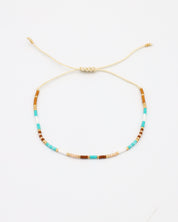 A beaded bracelet with a mix of gold and turquoise colors, featuring rhinestones and an adjustable cord.