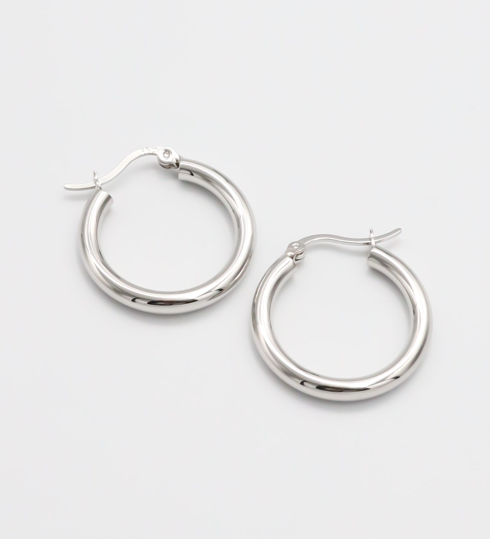 A pair of silver hoop earrings with a latch back closure on a white background