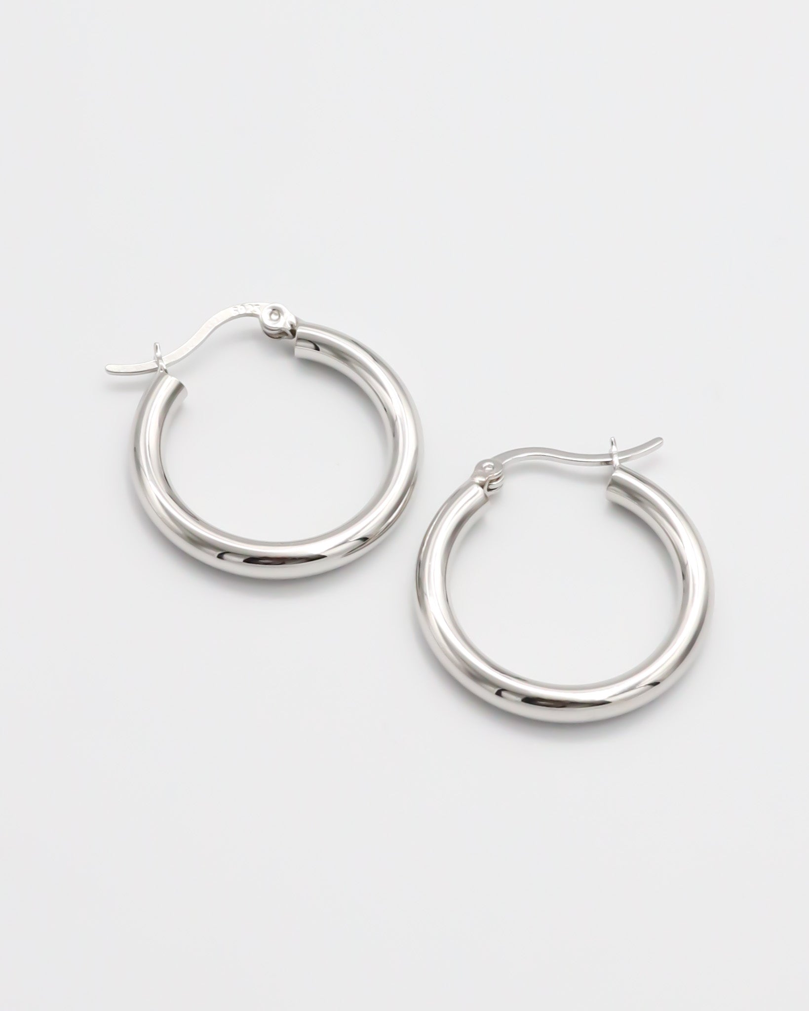 A pair of silver hoop earrings with a latch back closure on a white background