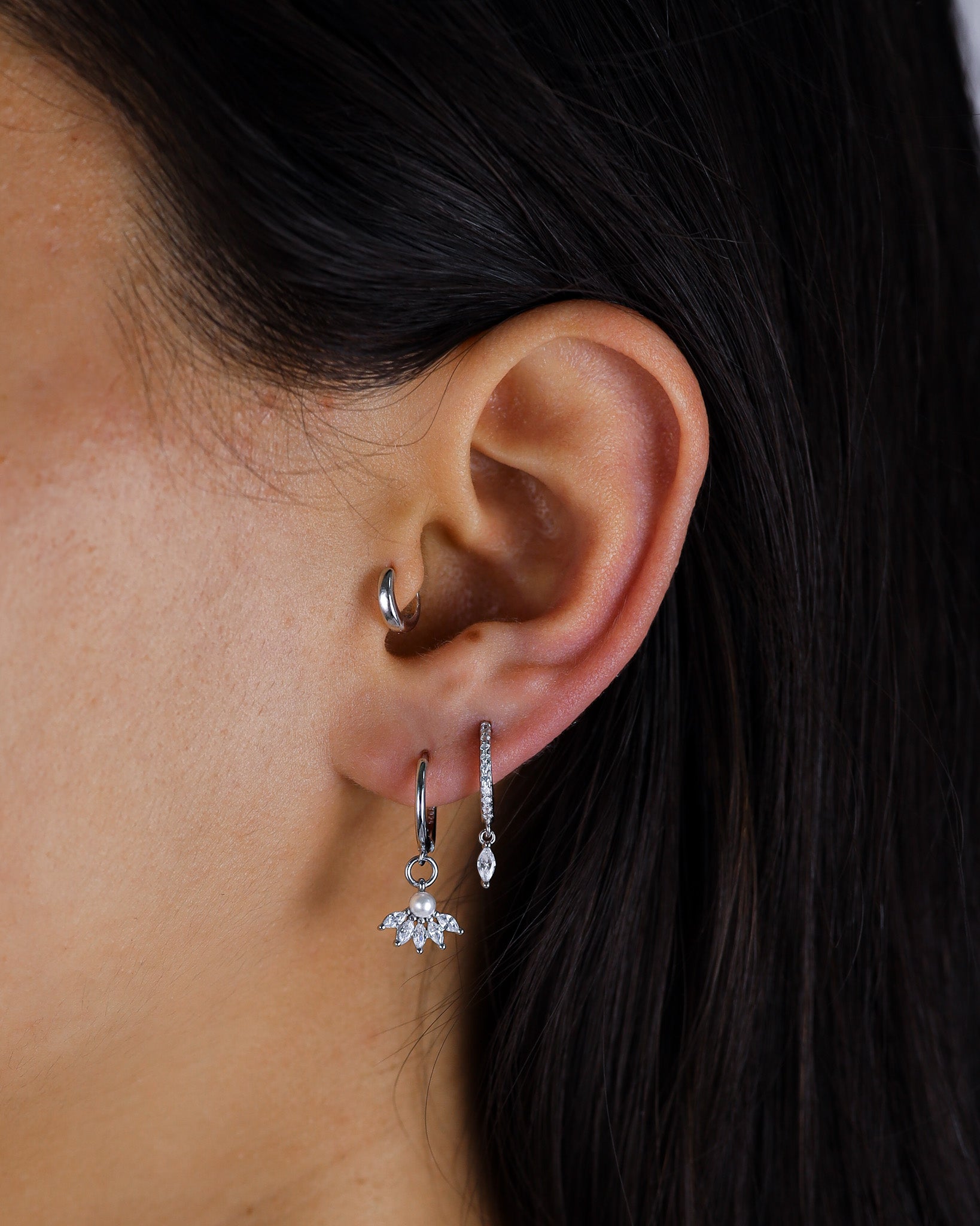 Close-up of an ear wearing silver hoop earrings with a dark background