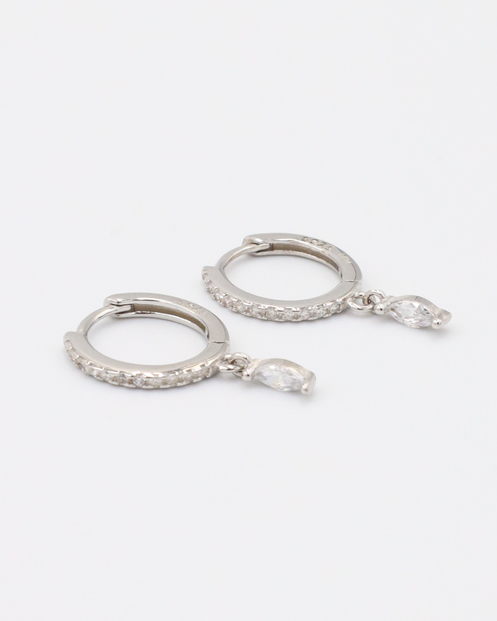 A silver-colored hoop earring with a small dangling gemstone attached, displayed against a white background.