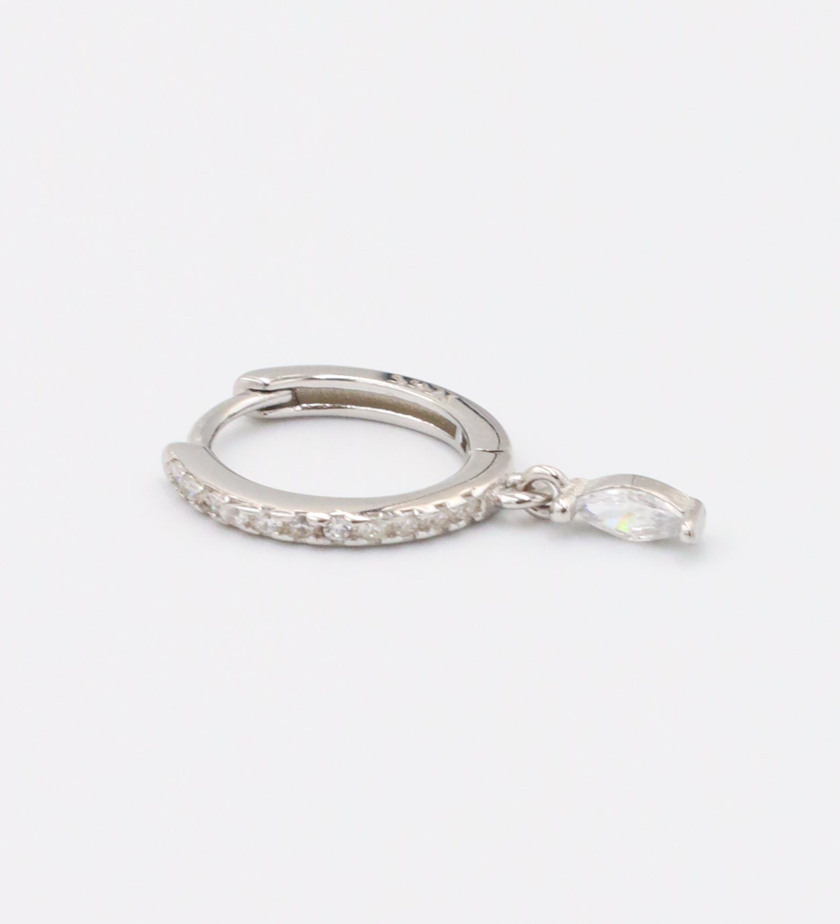 A silver-colored hoop earring with a small dangling gemstone attached, displayed against a white background.