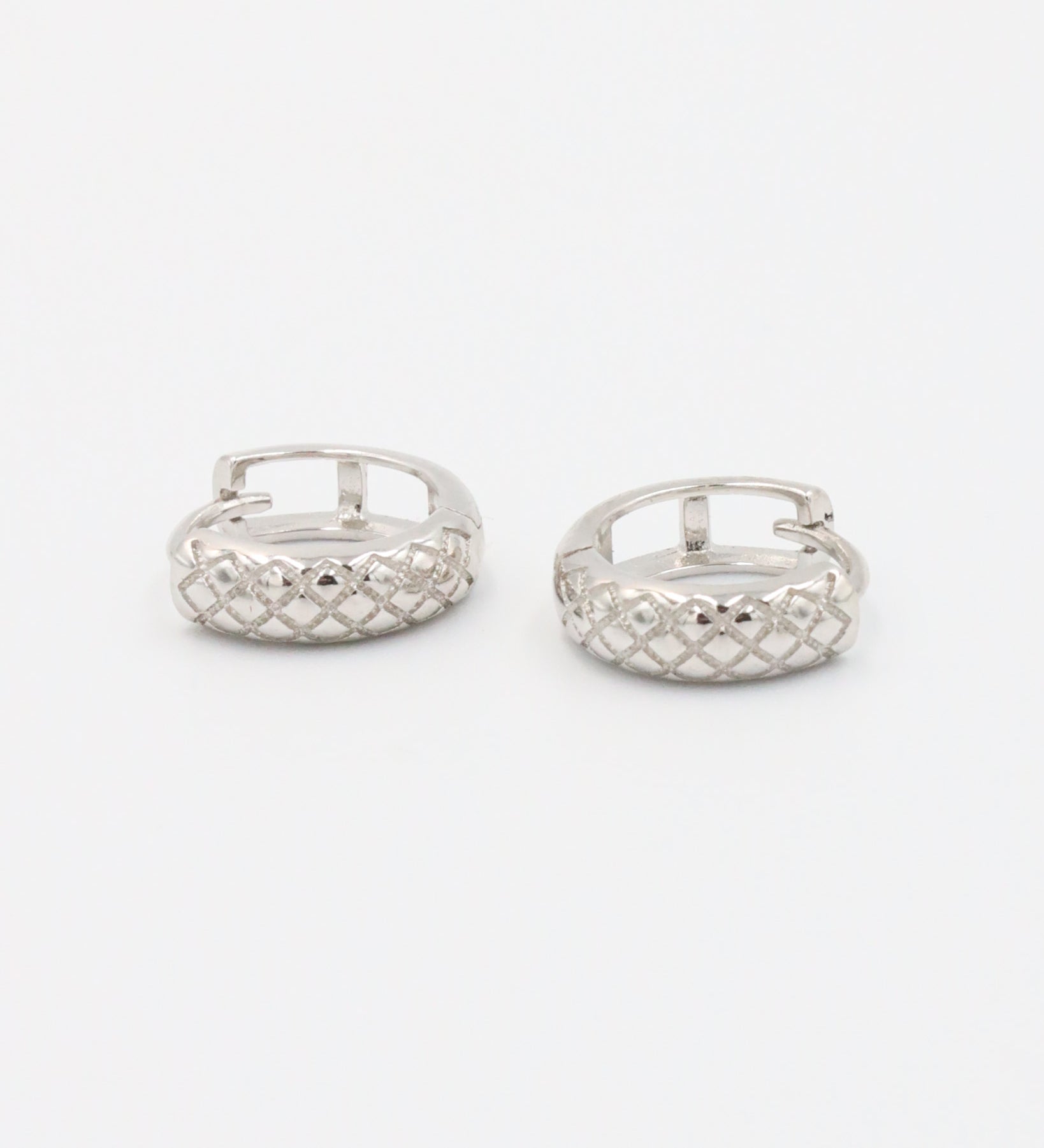 A single silver hoop earring with a geometric pattern and a hinged clasp.