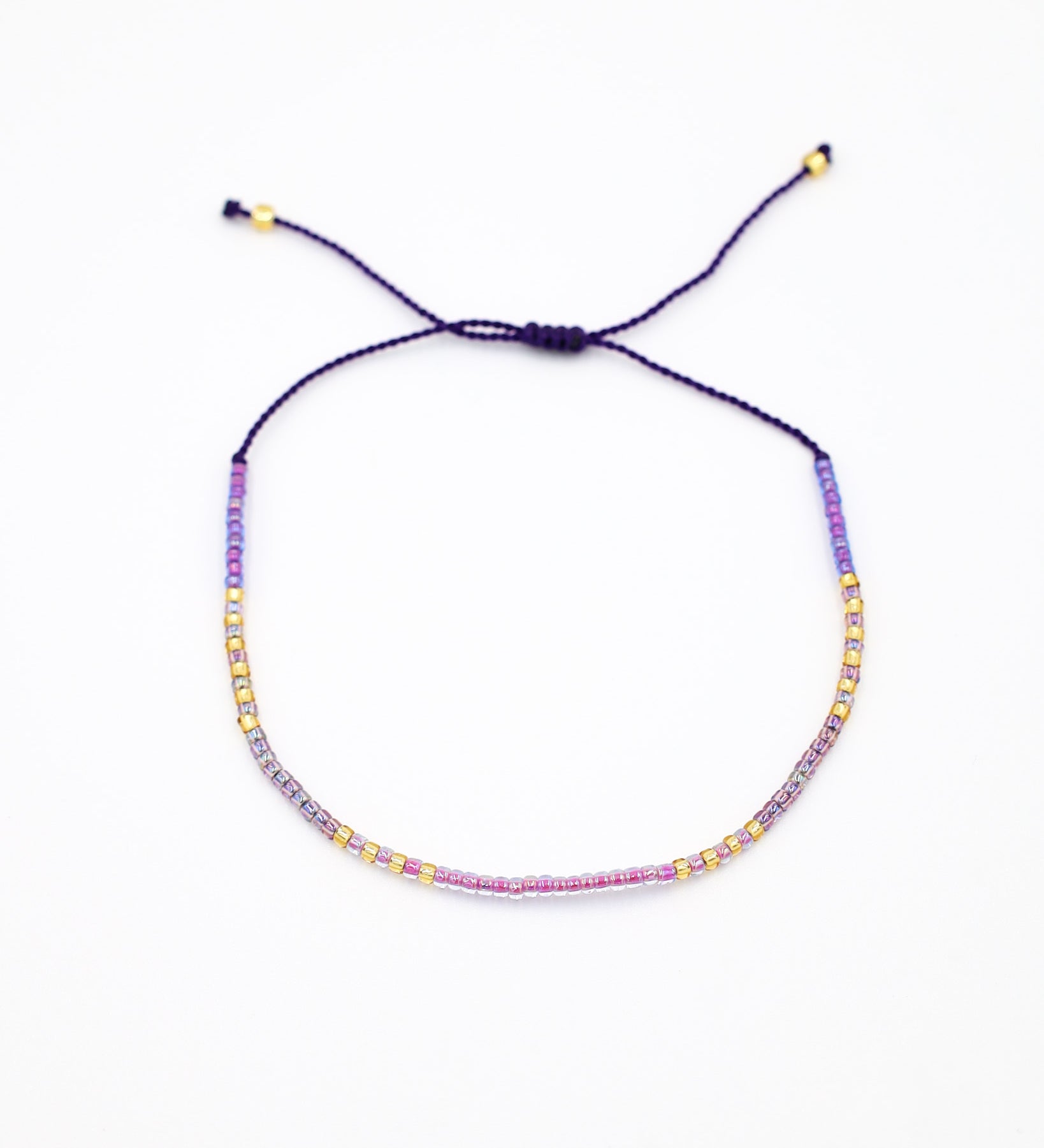 An adjustable gold-colored bracelet with a series of round beads and rhinestones strung on a dark strand.