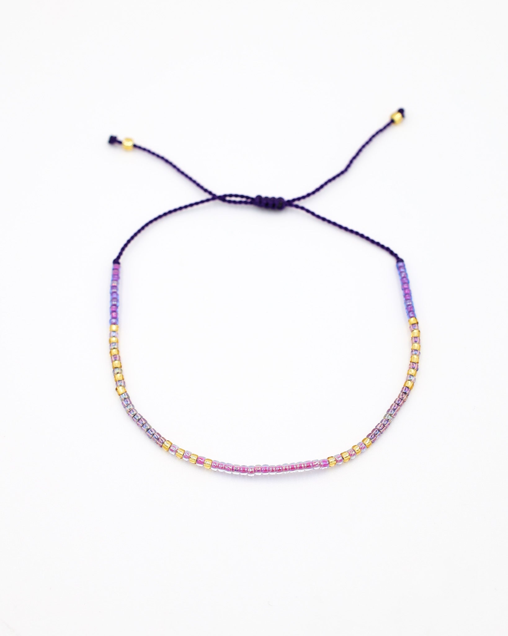 An adjustable gold-colored bracelet with a series of round beads and rhinestones strung on a dark strand.