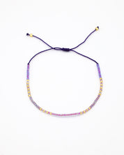 An adjustable gold-colored bracelet with a series of round beads and rhinestones strung on a dark strand.