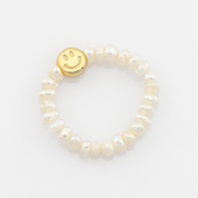 Pearl ring with a gold smiley face charm on a light gray background
