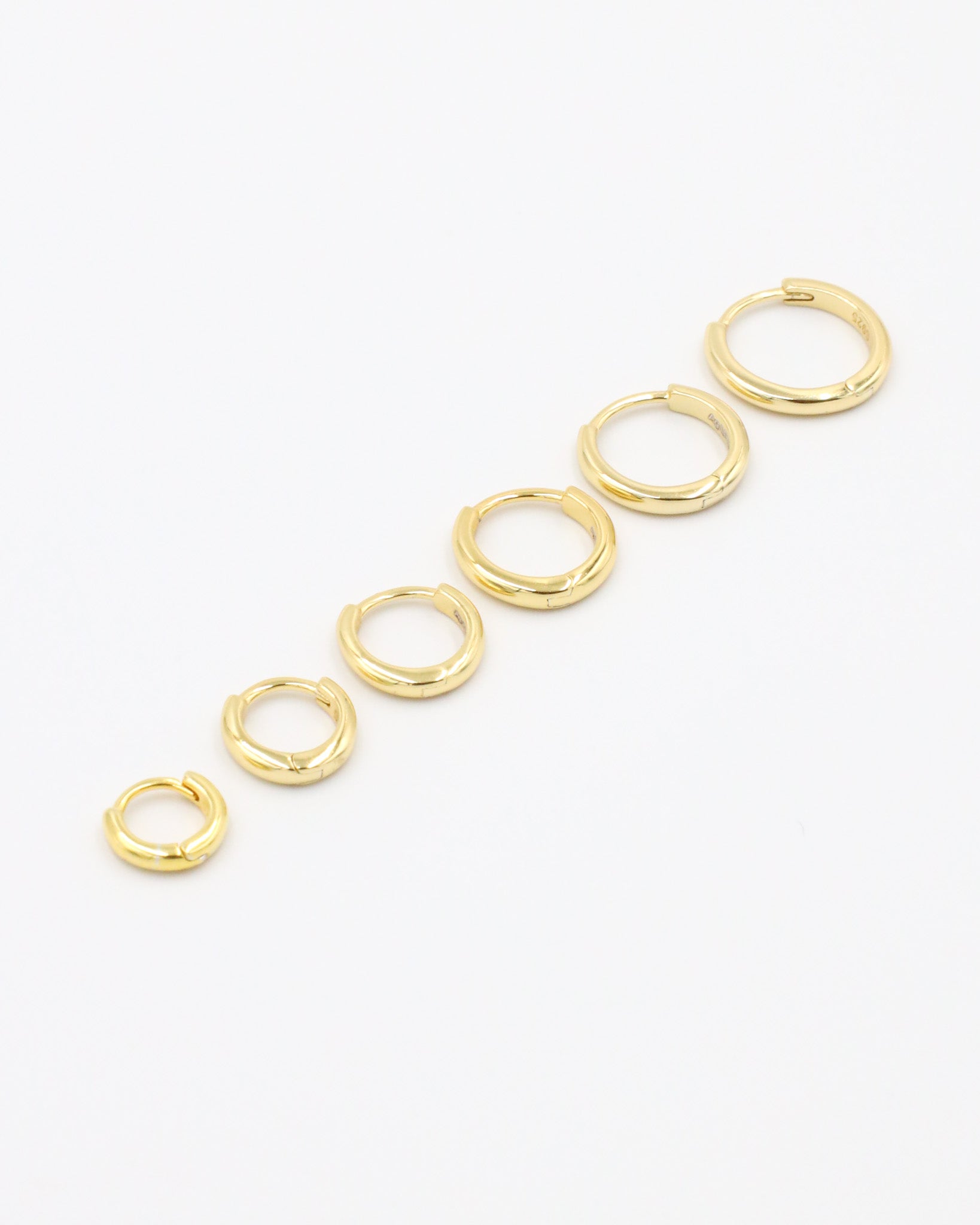 A series of circular gold colored hoops of varying sizes arranged in a line on a white background.