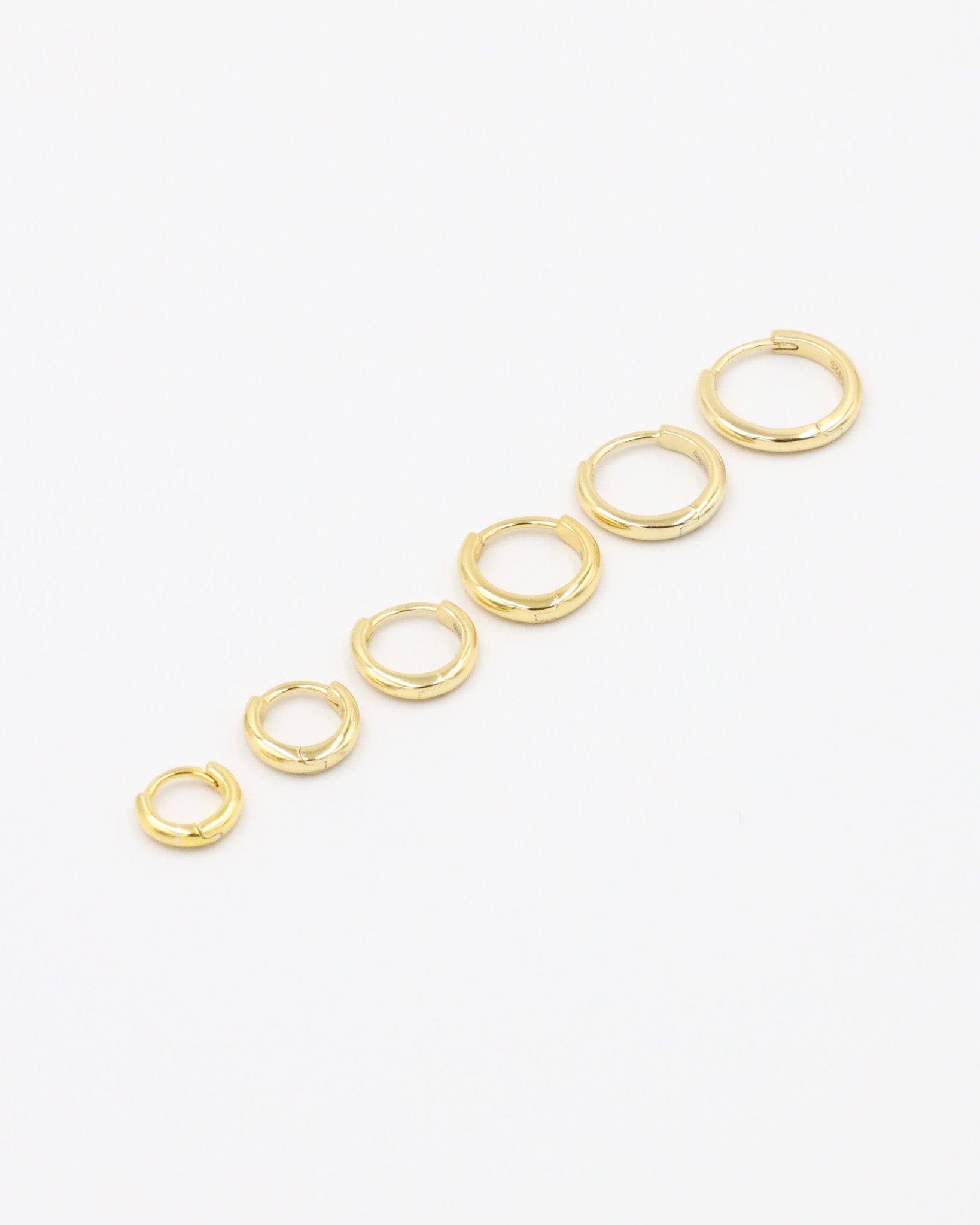 A series of circular gold colored hoops of varying sizes arranged in a line on a white background.