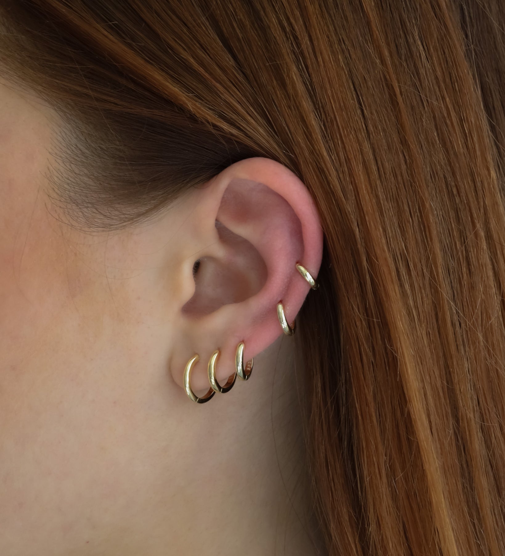 Close-up of an ear wearing six Lu Earrings in different sizes, styled across multiple piercings for a stacked and minimal look.