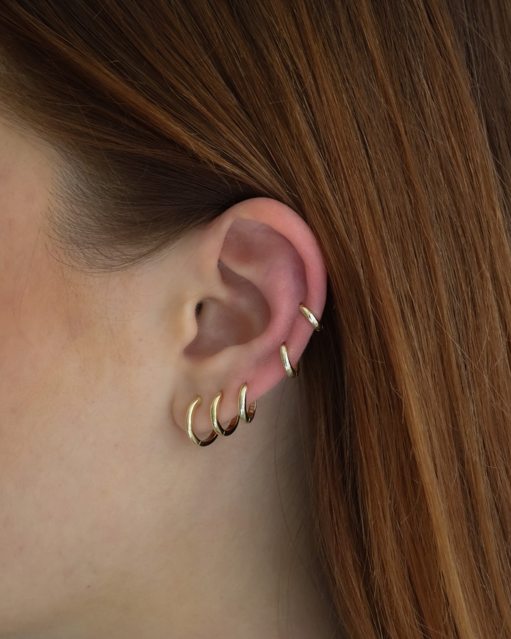 Close-up of an ear wearing six Lu Earrings in different sizes, styled across multiple piercings for a stacked and minimal look.