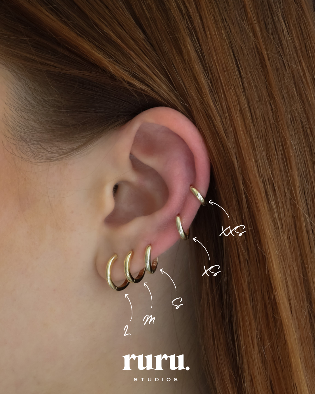 Close-up of an ear wearing six Lu Earrings in different sizes, styled across multiple piercings for a stacked and minimal look.