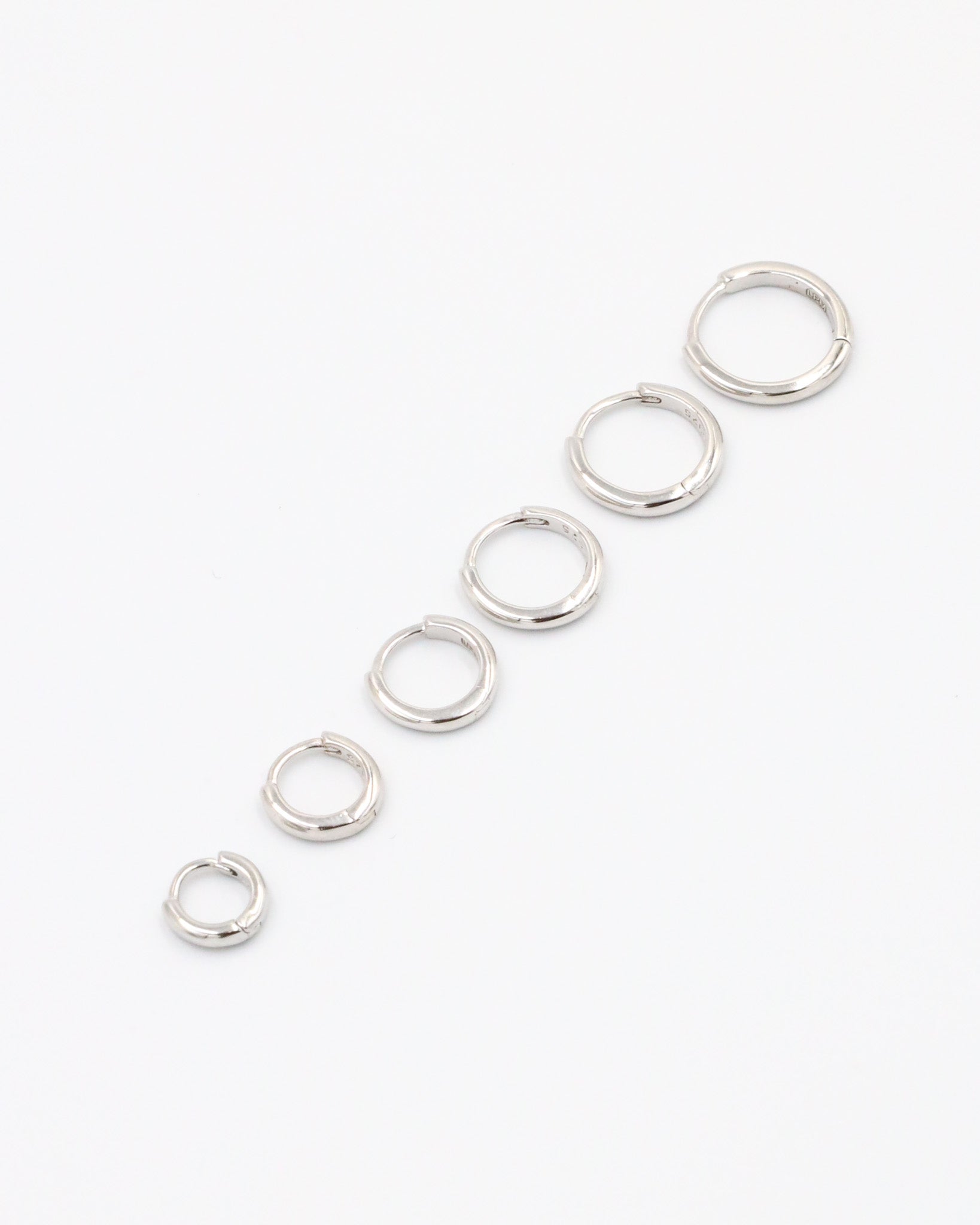 A series of circular silver hoops of varying sizes arranged in a line on a white background.