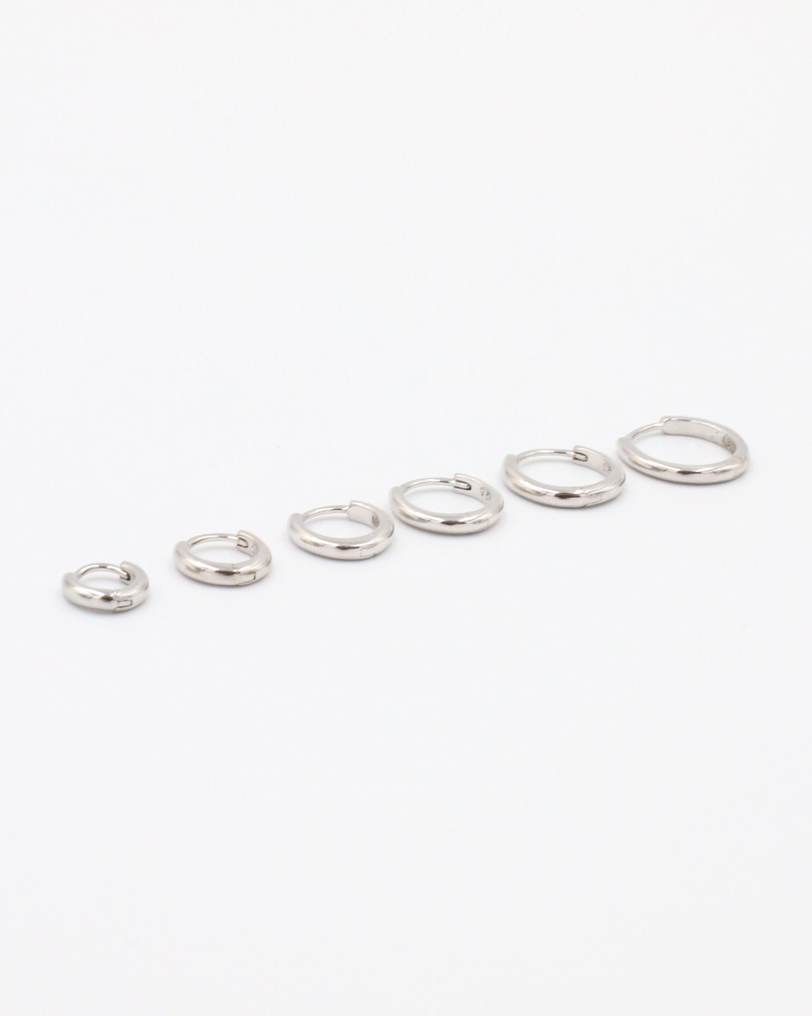A series of circular silver colored hoops of varying sizes arranged in a line on a white background.