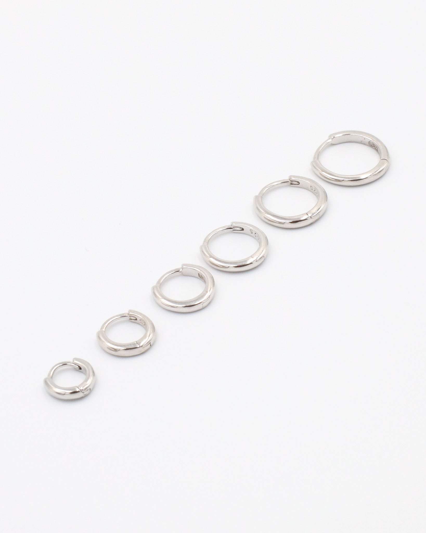 A series of circular silver colored hoops of varying sizes arranged in a line on a white background.