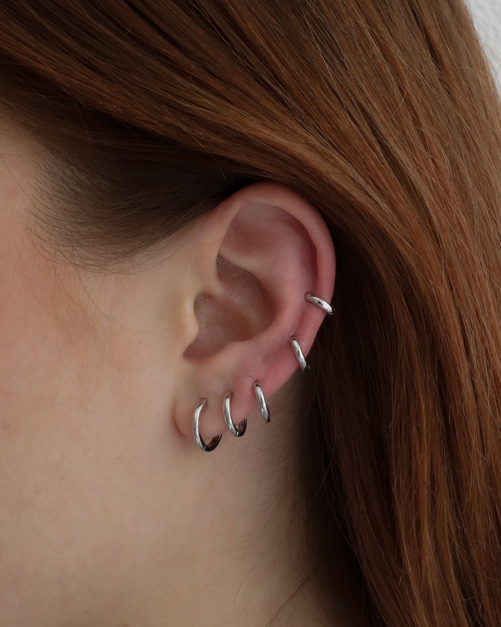 Close-up of an ear wearing six Lu Earrings in different sizes, styled across multiple piercings for a stacked and minimal look.