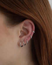 Close-up of an ear wearing six Lu Earrings in different sizes, styled across multiple piercings for a stacked and minimal look.