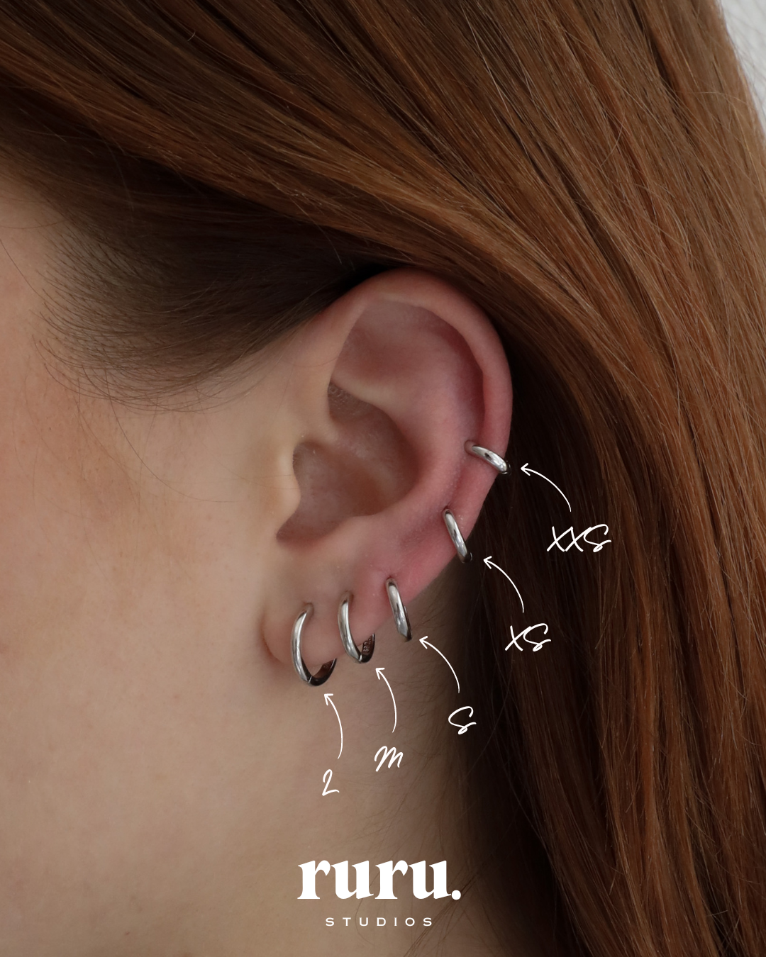 Close-up of an ear wearing six Lu Earrings in different sizes, styled across multiple piercings for a stacked and minimal look.