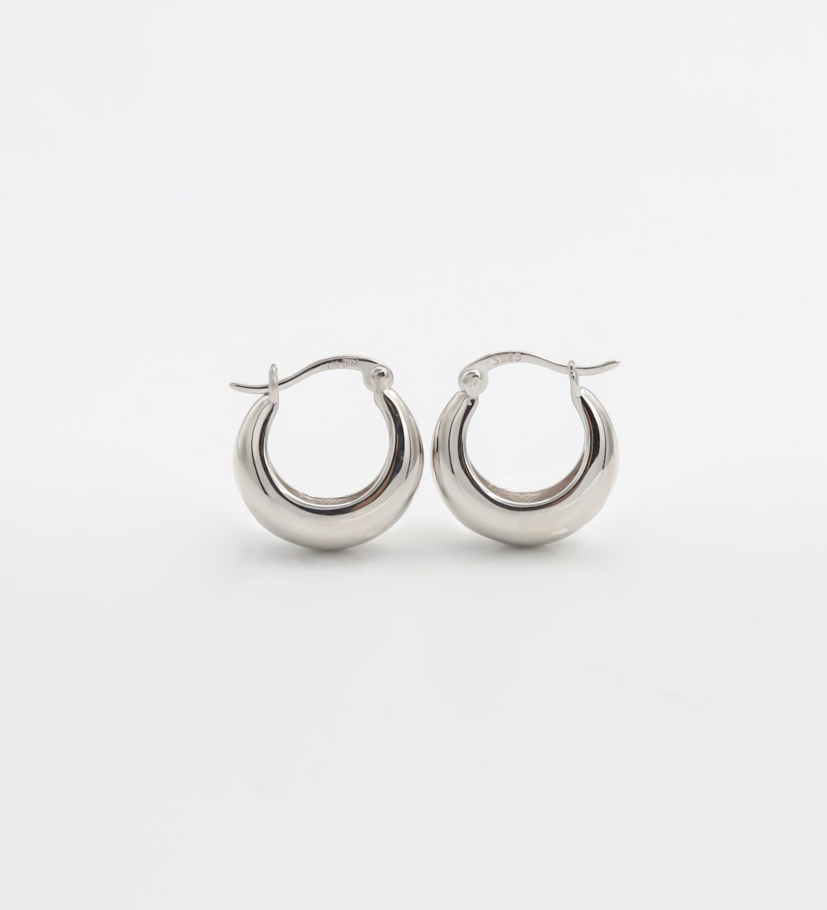 A pair of silver hoop earrings with a latch back closure on a white background