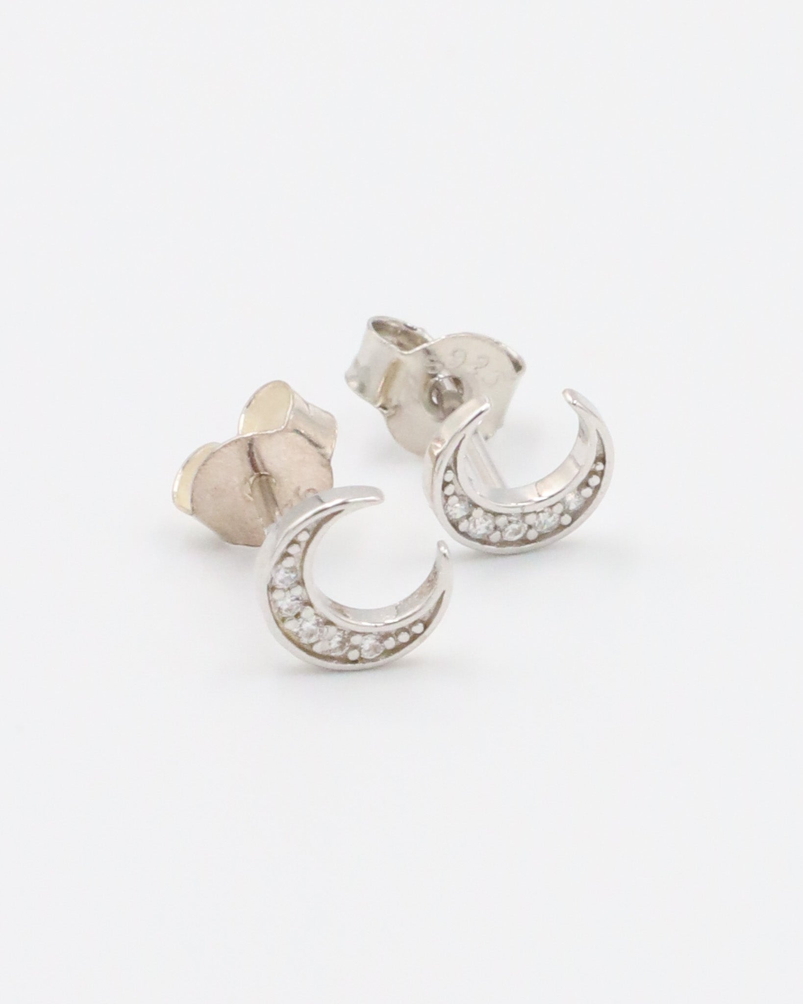 A single silver-colored earrings with a crescent shape and small, embedded stones, displayed against a white background.