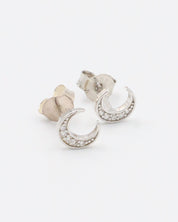 A single silver-colored earrings with a crescent shape and small, embedded stones, displayed against a white background.