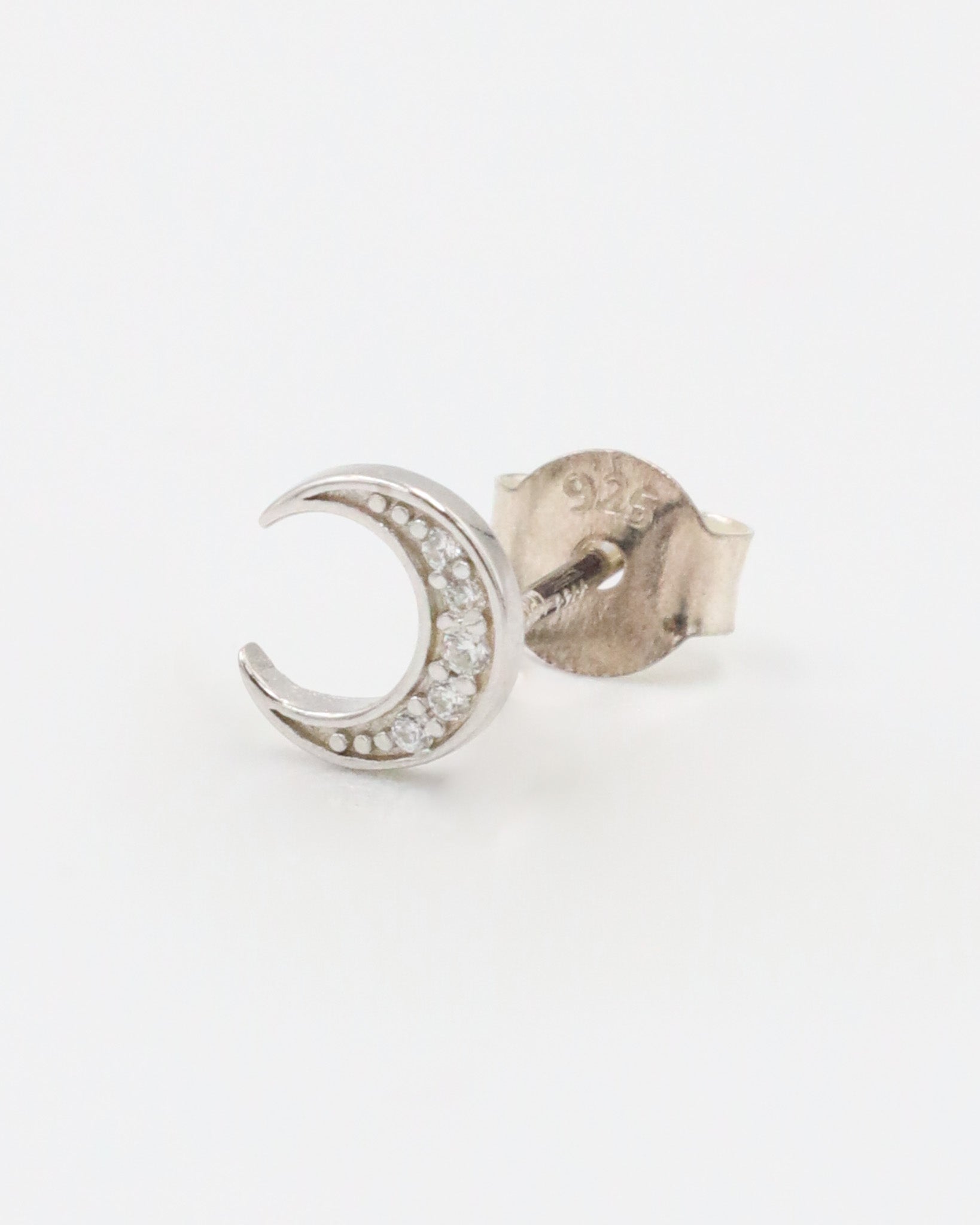 A single silver-colored earrings with a crescent shape and small, embedded stones, displayed against a white background.