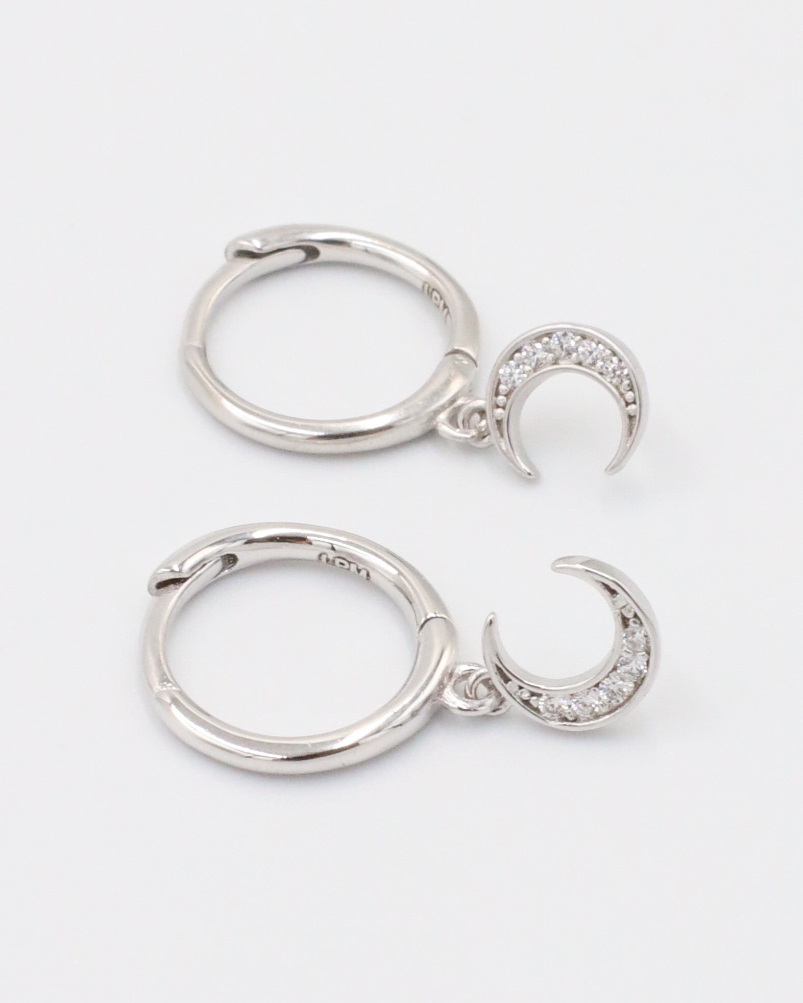 A silver hoop earring with a crescent moon charm attached, displayed against a white background.