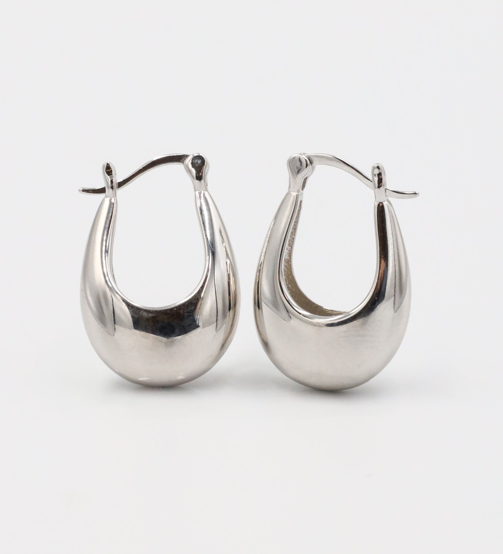 This image displays a pair of elegant silver earrings, referred to as the Marigold Silver piece. The earrings feature a sleek, polished design with a smooth, curved structure that reflects light beautifully.