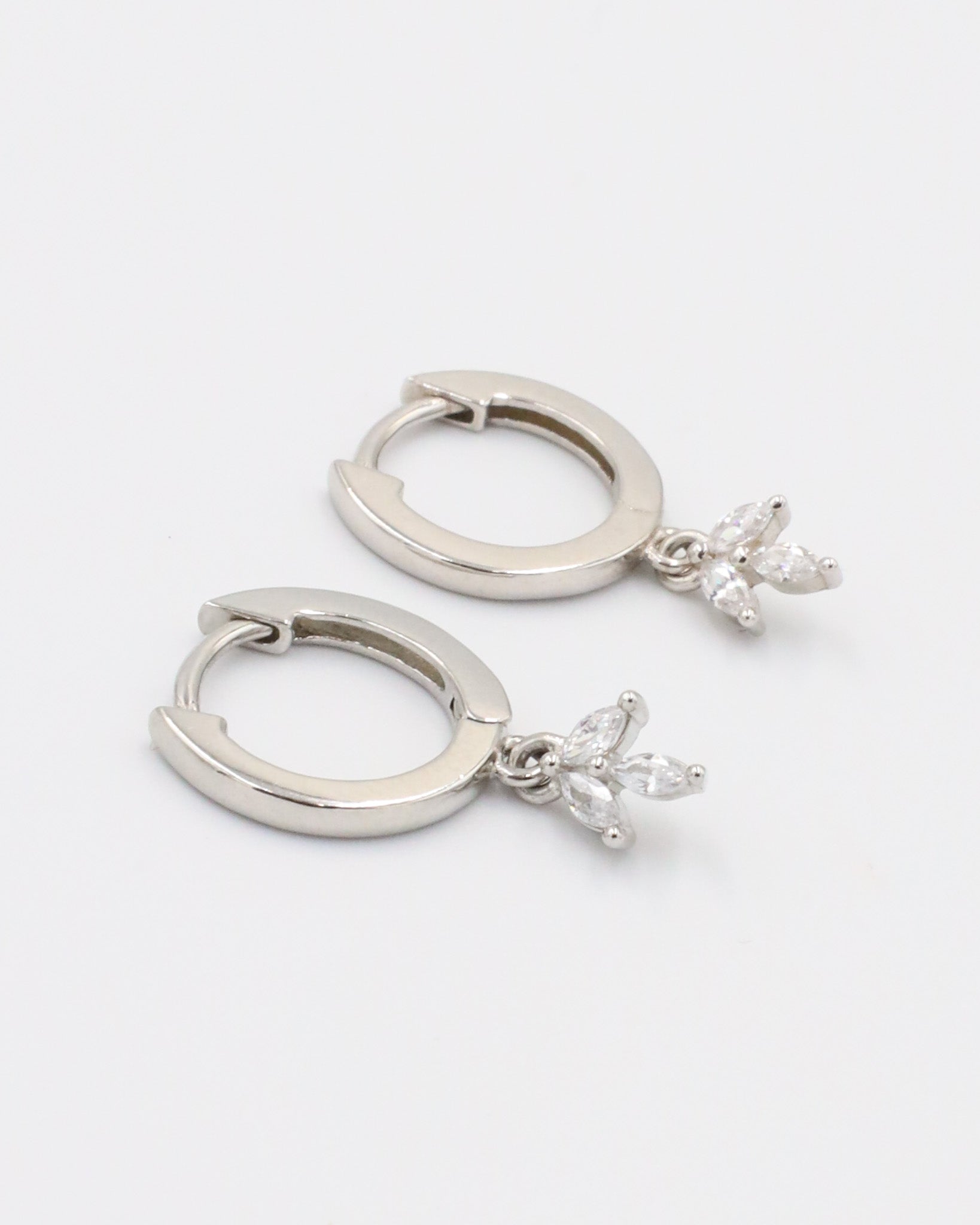 A silver-colored hoop earring with a hinged clasp and a dangling decorative element.