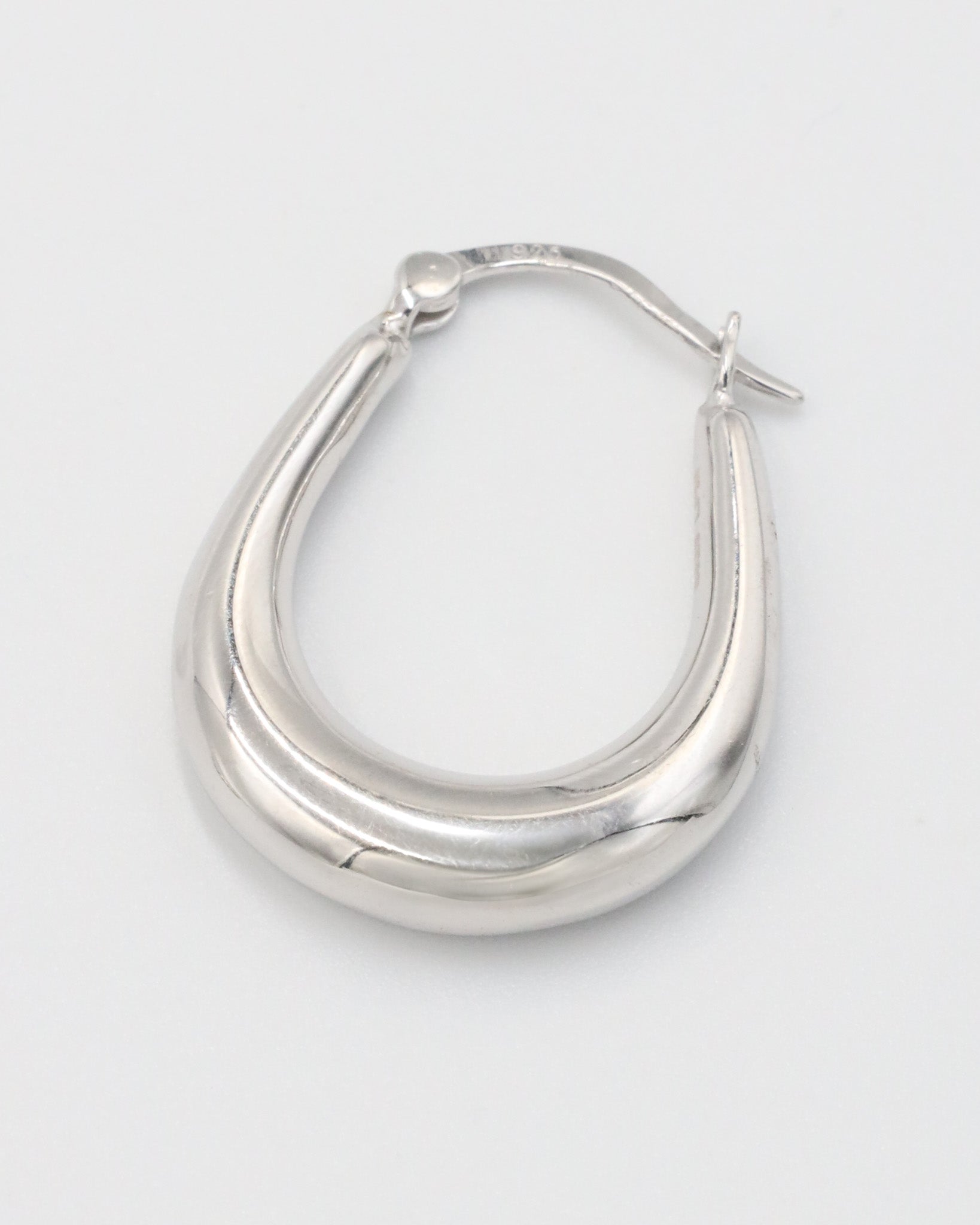 A pair of silver hoop earrings with a latch back clasp on a white background.