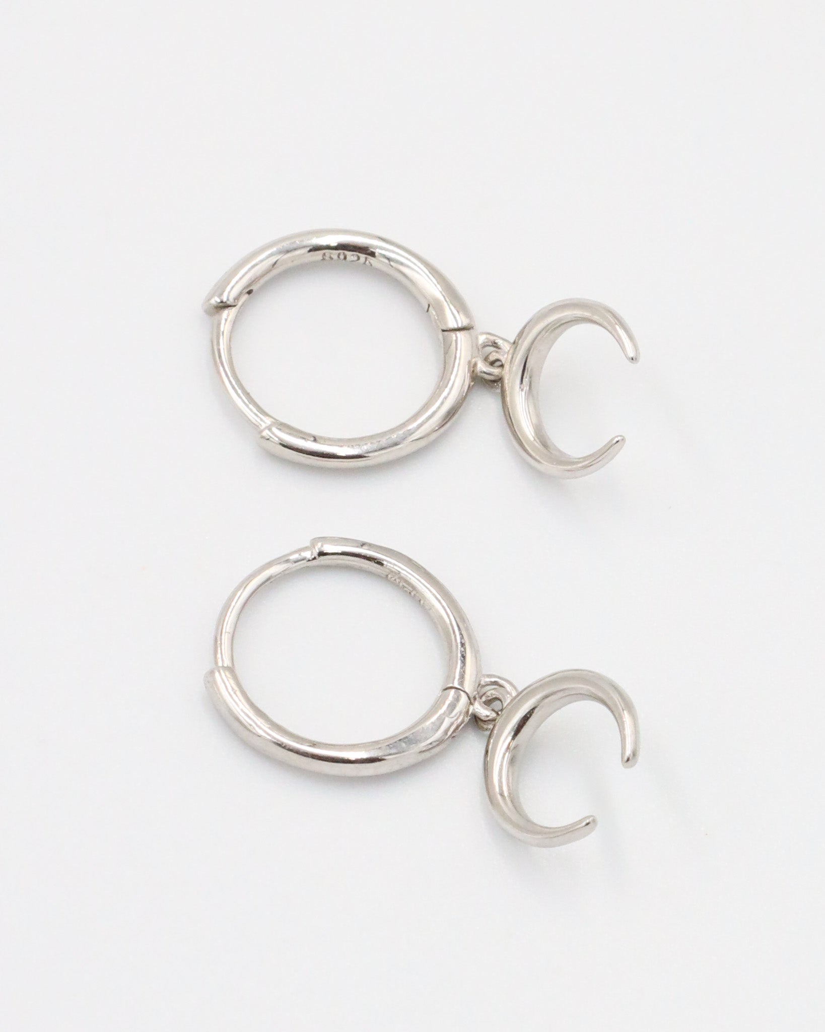 A silver-colored hoop earring with a hinged clasp and a small crescent moon charm attached to it.