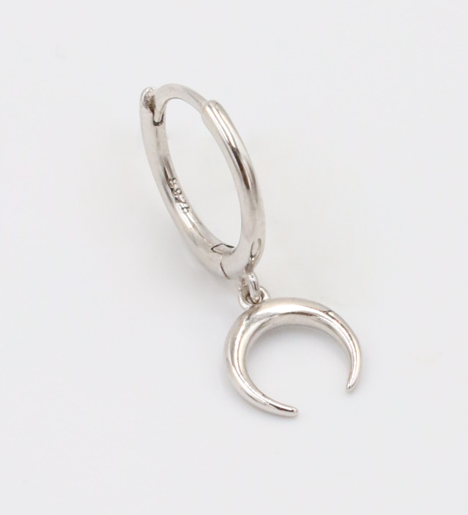 A silver-colored hoop earring with a hinged clasp and a small crescent moon charm attached to it.