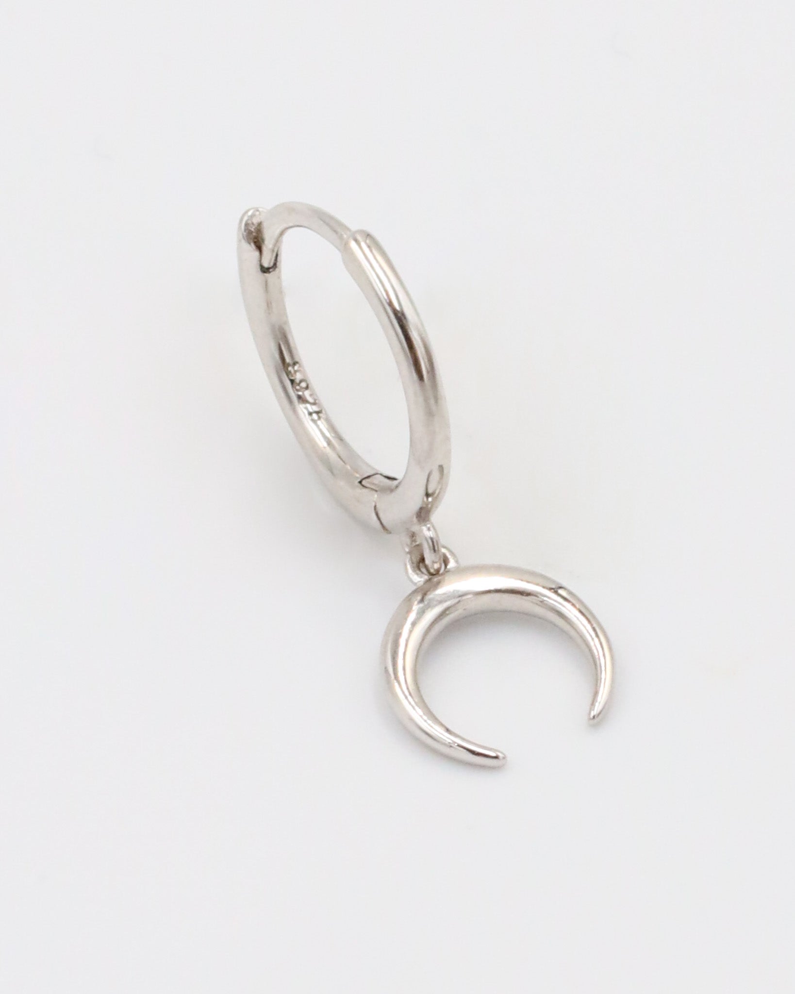 A silver-colored hoop earring with a hinged clasp and a small crescent moon charm attached to it.