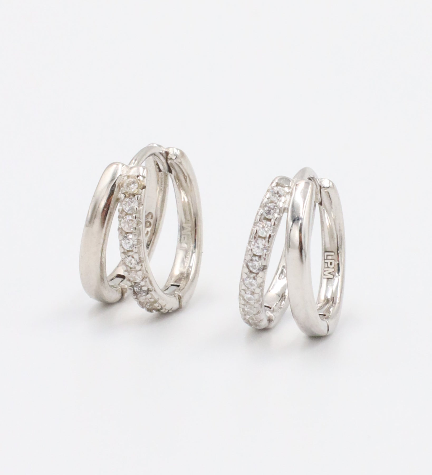 A pair of silver hoop earrings with a hinged clasp closure, featuring a row of small clear stones on the hoop.