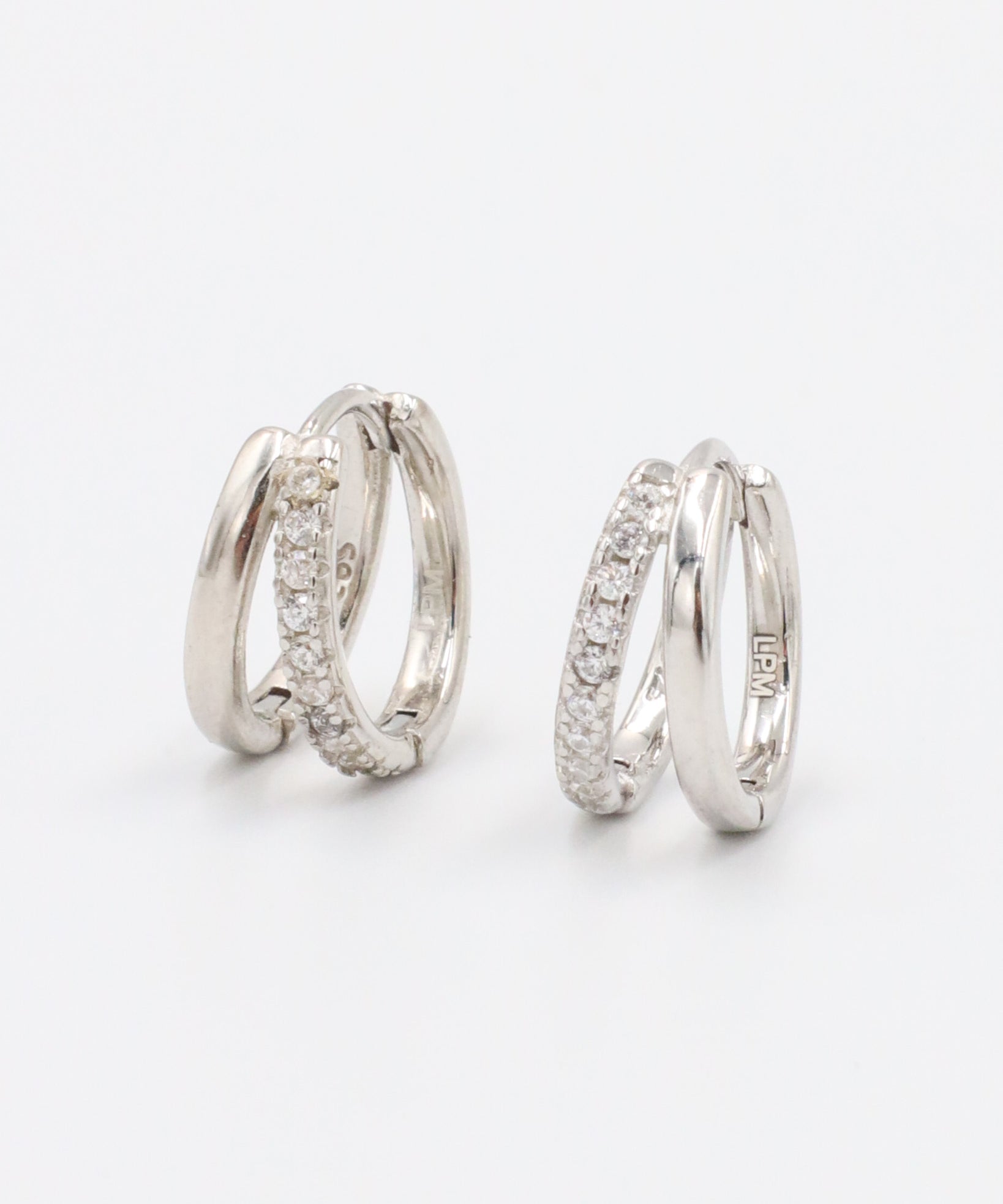 A pair of silver hoop earrings with a hinged clasp closure, featuring a row of small clear stones on the hoop.