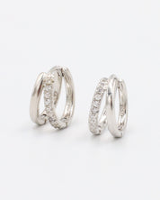 A pair of silver hoop earrings with a hinged clasp closure, featuring a row of small clear stones on the hoop.