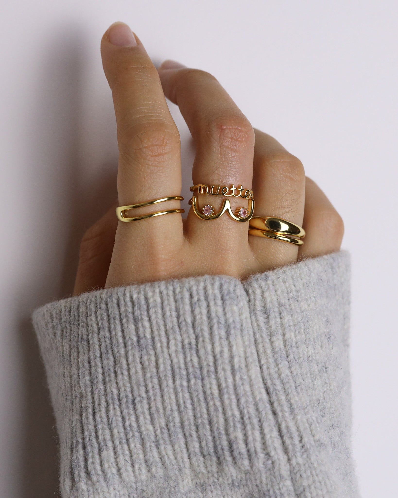Hand wearing multiple gold rings with a neutral background