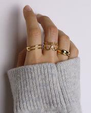 Hand wearing multiple gold rings with a neutral background
