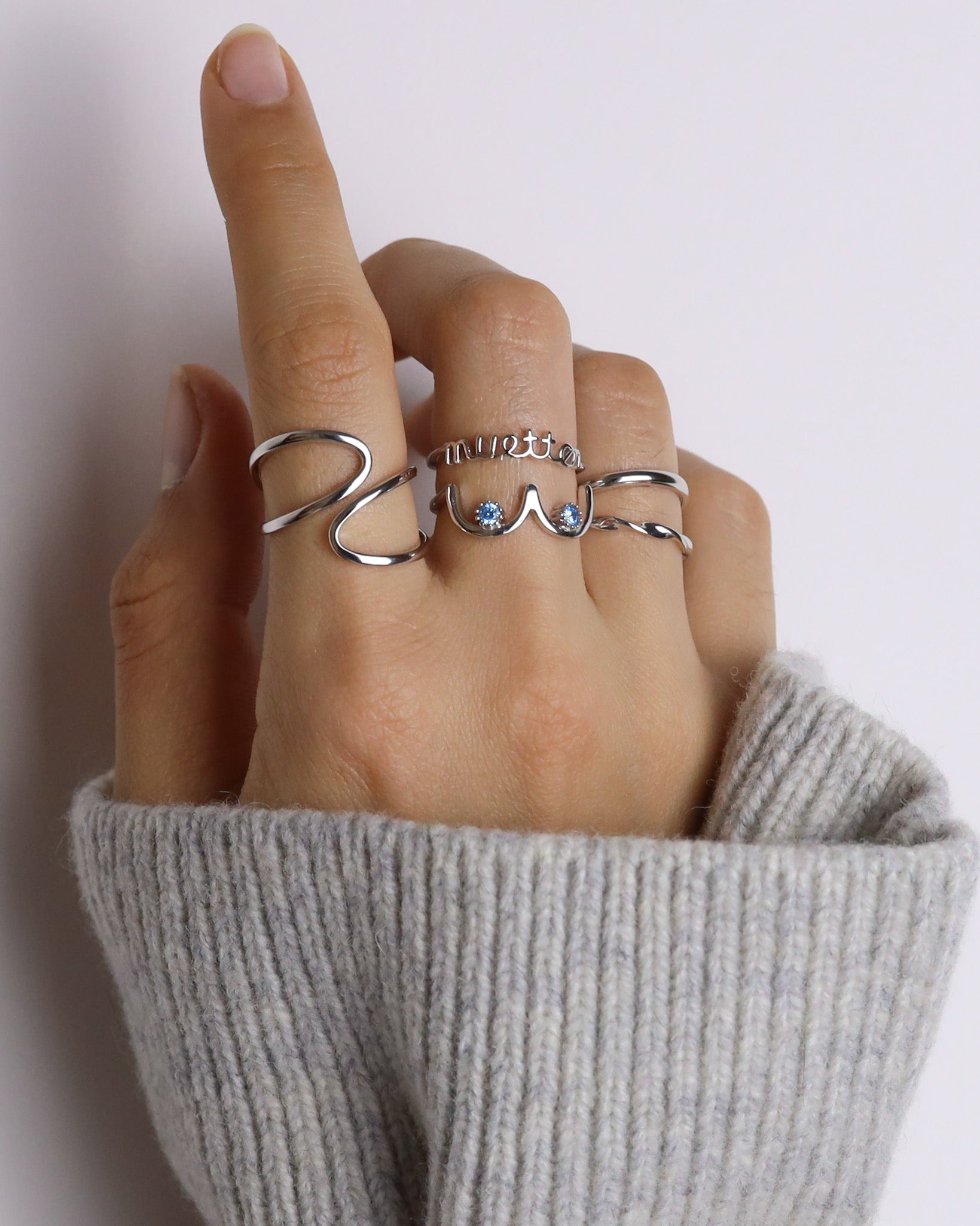 Hand wearing multiple silver rings on a plain background