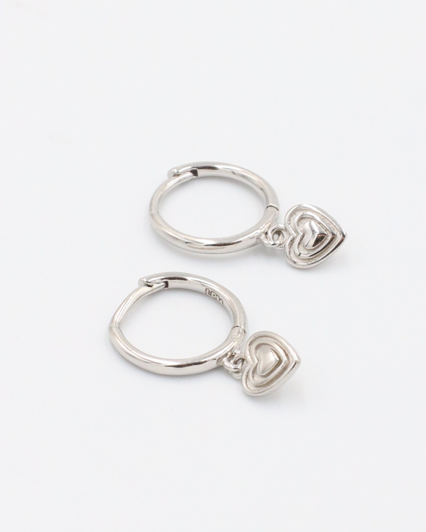 A silver-colored ring with a small heart-shaped charm attached to it, displayed against a white background.