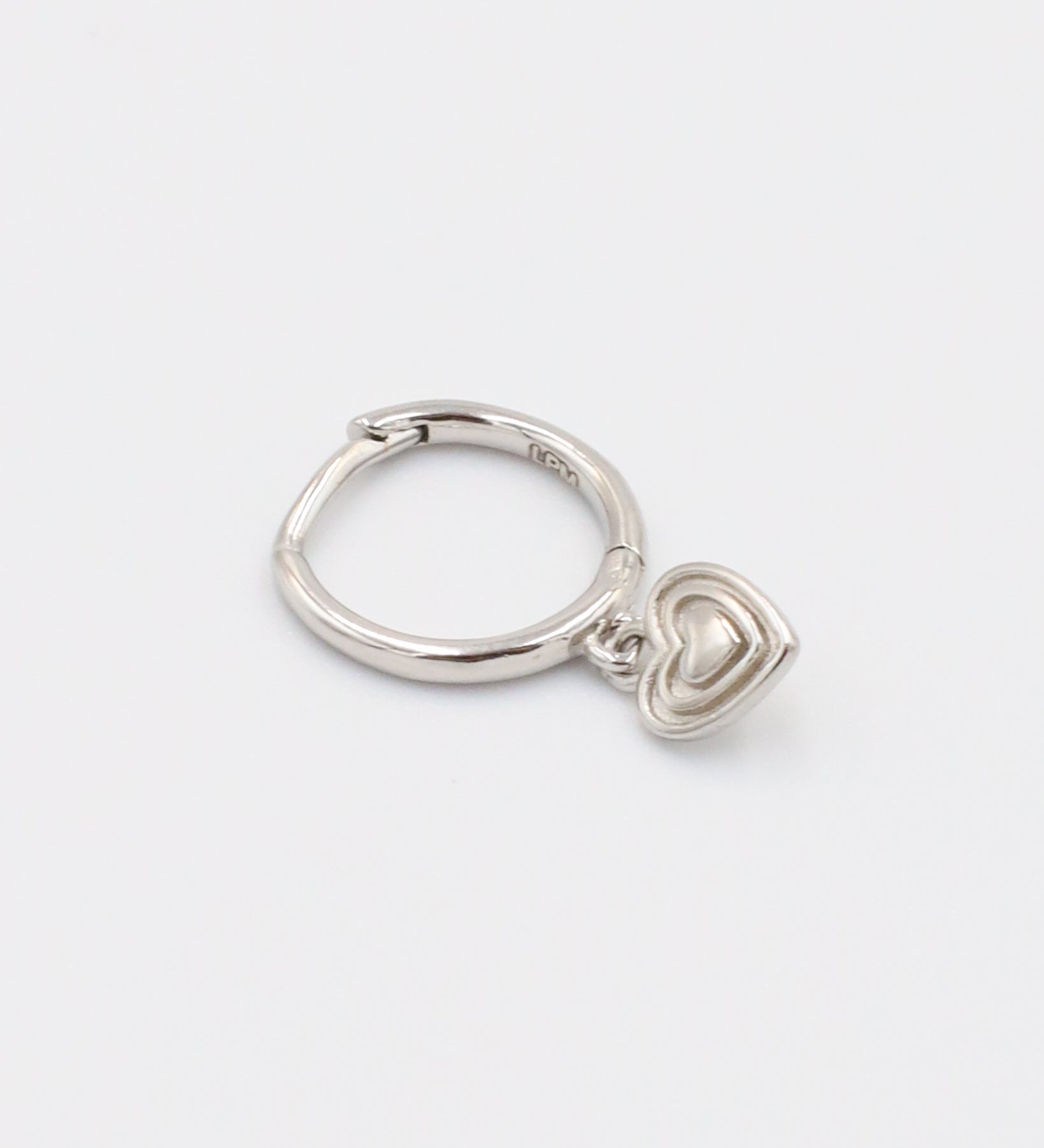 A silver-colored ring with a small heart-shaped charm attached to it, displayed against a white background.