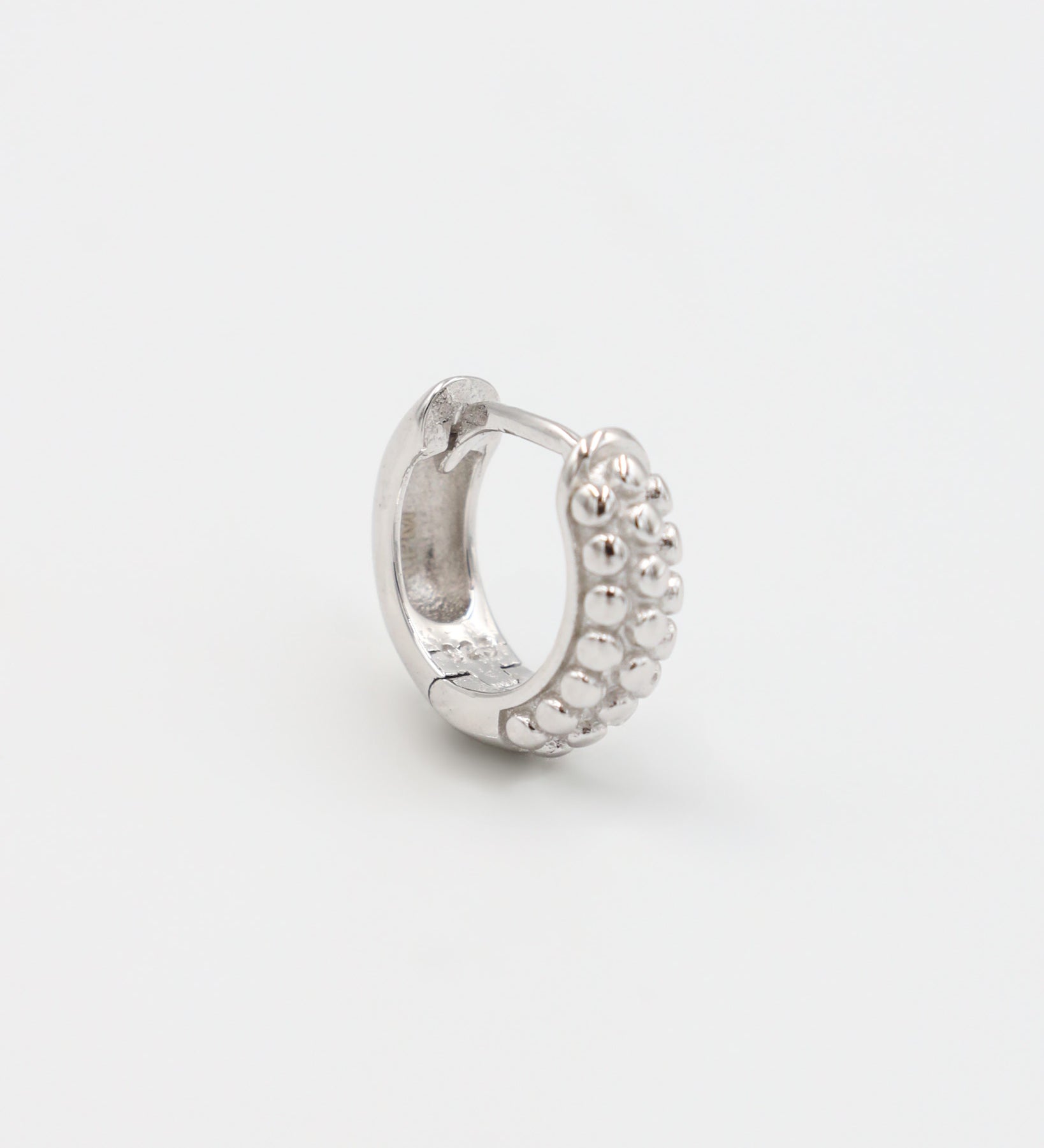 A single silver hoop earring with a pressure system anchoring and small decorative stones around the edge.