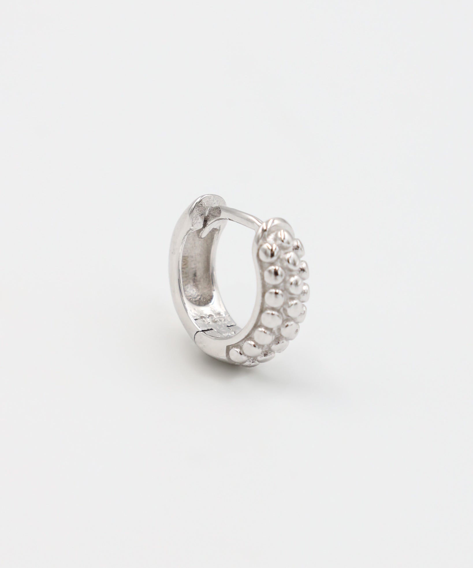 A single silver hoop earring with a pressure system anchoring and small decorative stones around the edge.