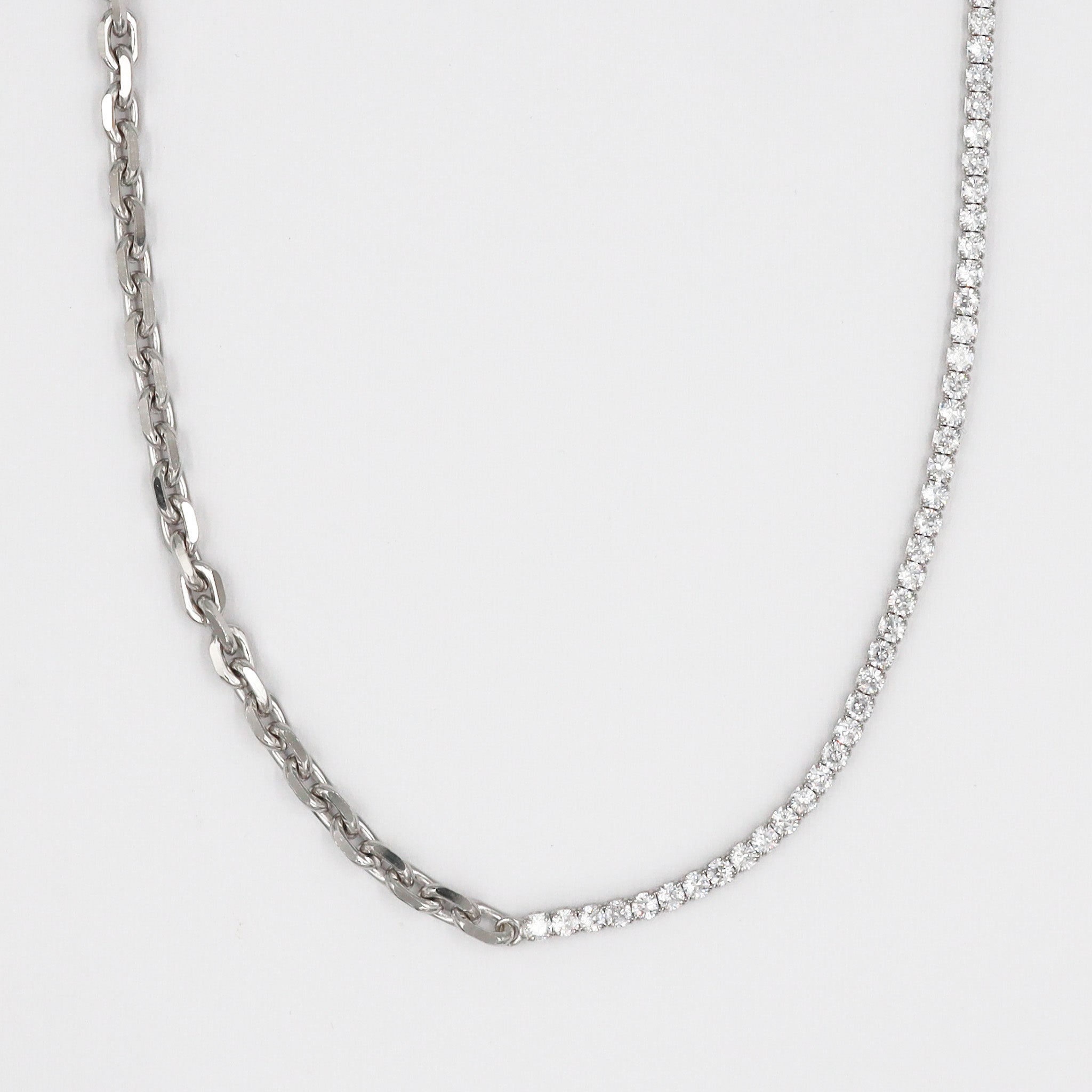A silver necklace with a twisted rope chain design laid out on a plain surface.